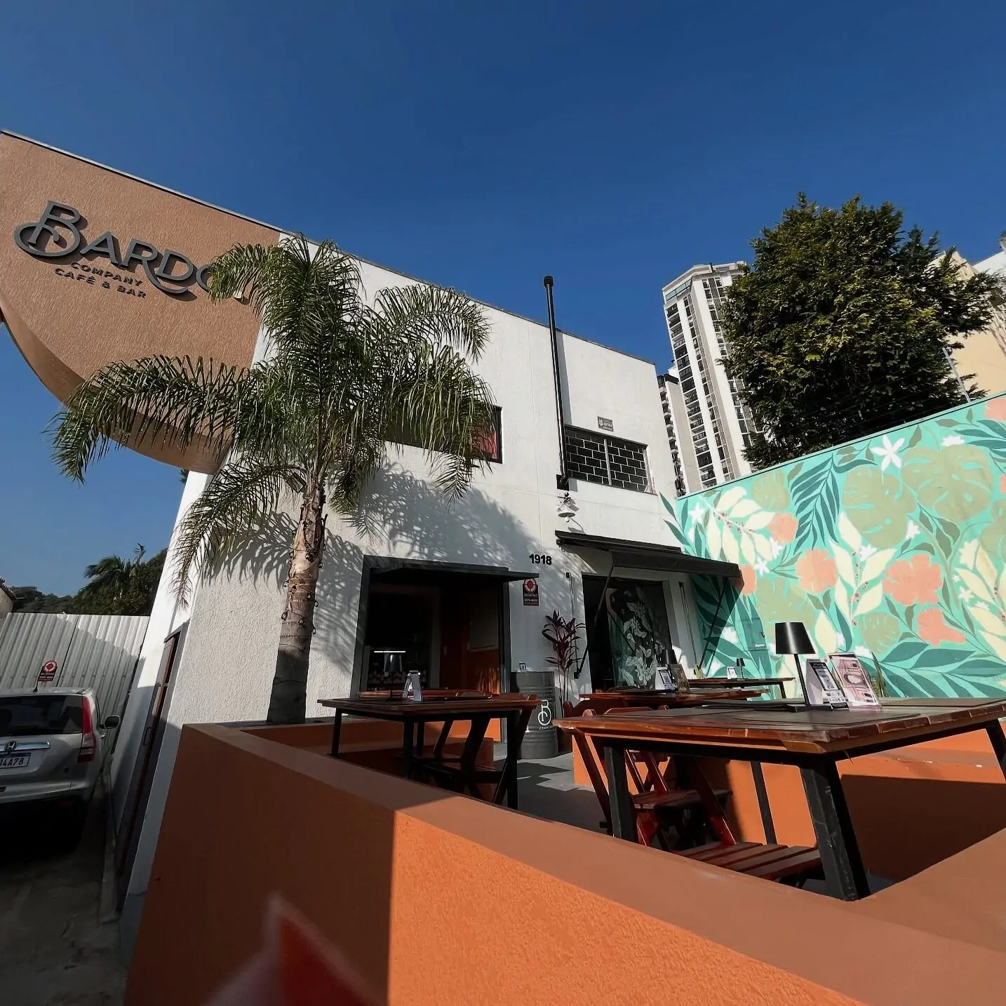 Fachada do Bardo Café & Bar em Curitiba, com mesas ao ar livre, mural colorido e céu azul claro